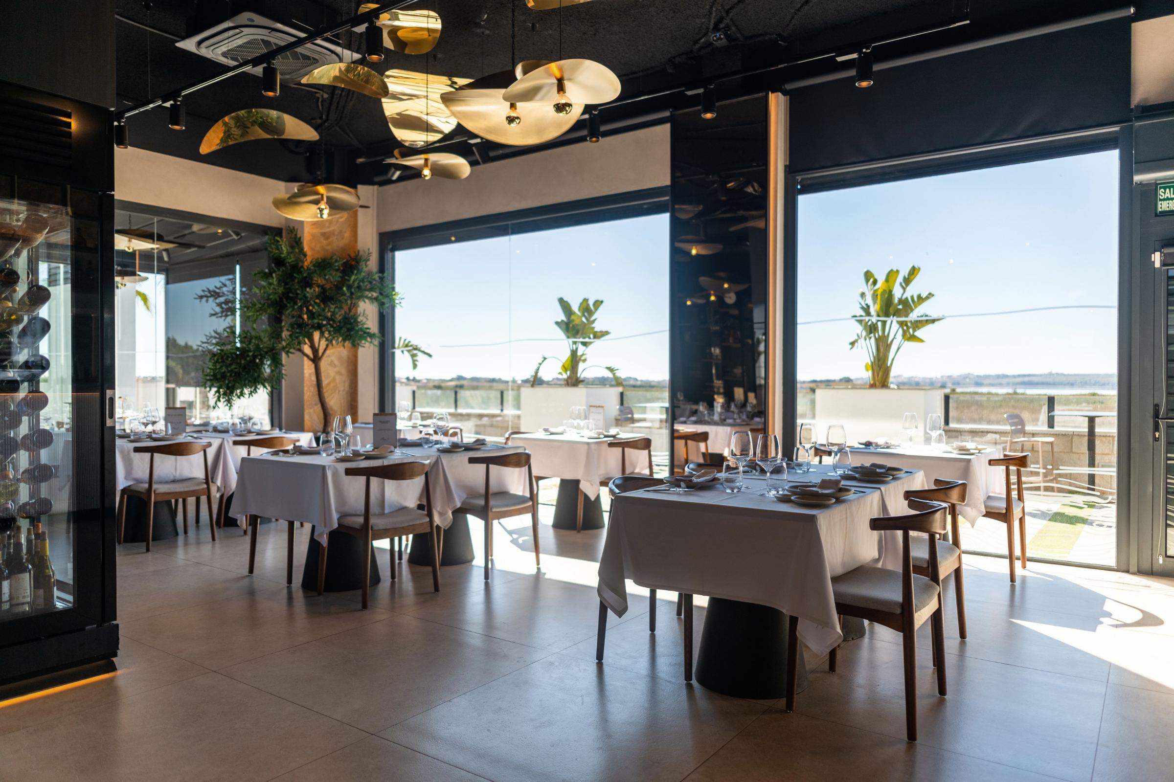 Comedor luminoso con mesas vestidas de blanco, ventanales y lámparas doradas