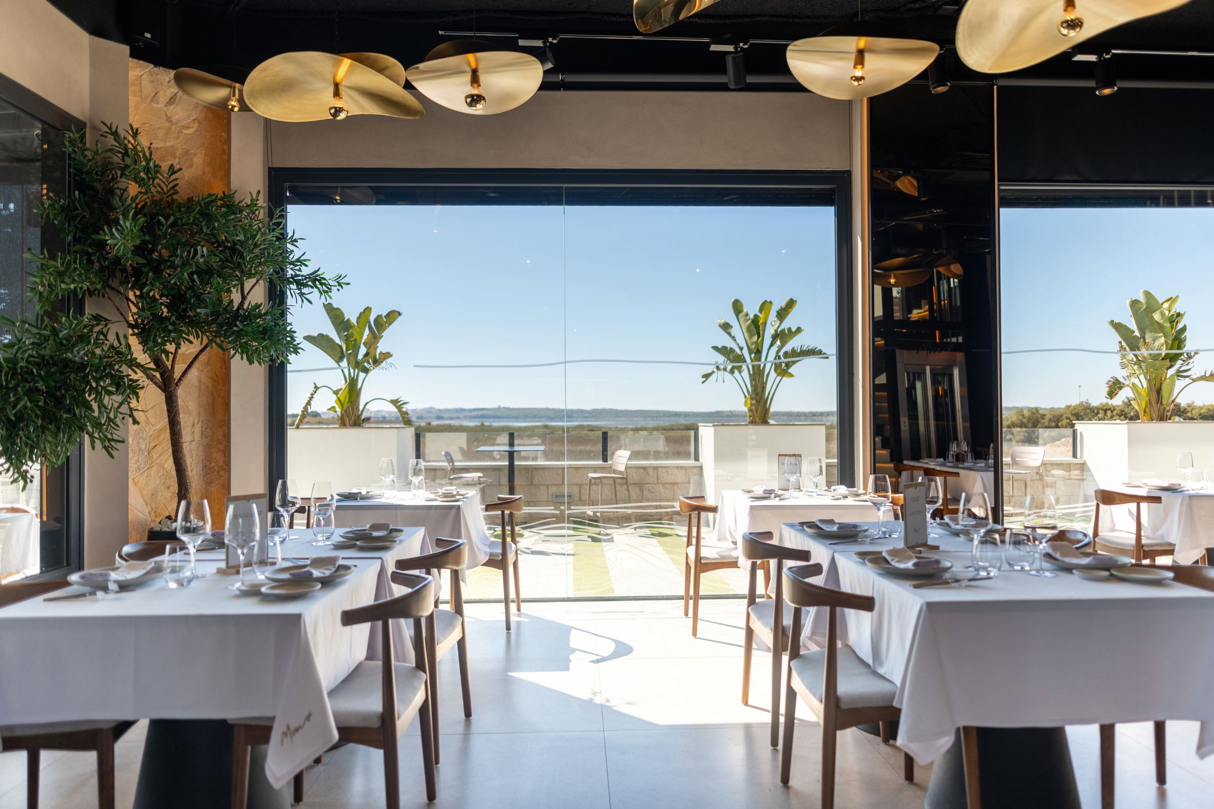 Comedor de Mimo con mesas vestidas de blanco frente a un gran ventanal con vistas a las salinas