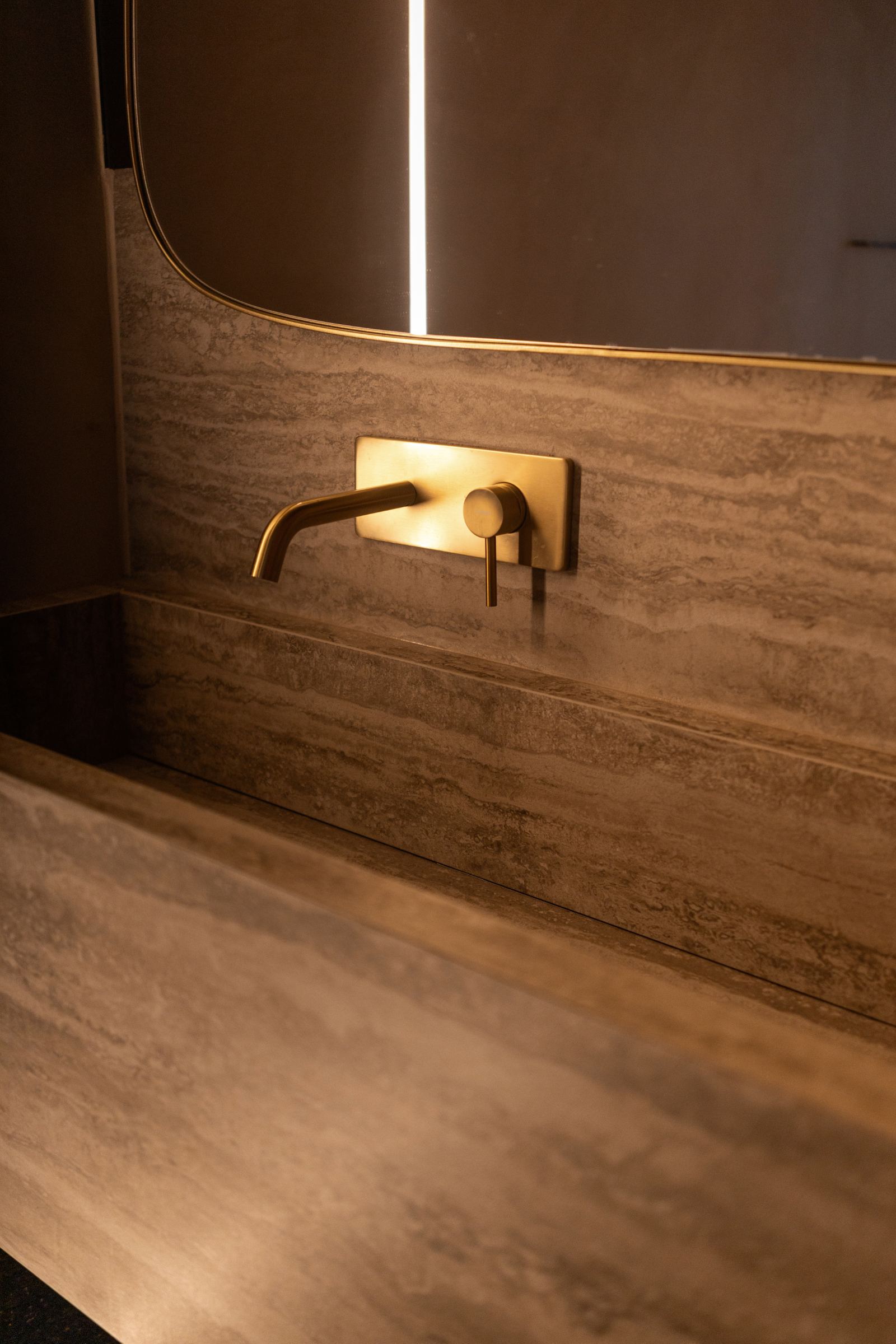 Detalle de grifería dorada sobre lavabo de piedra travertino