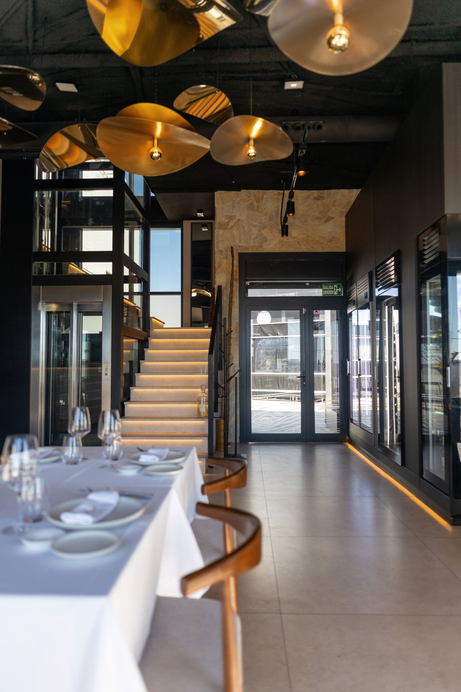 Escalera iluminada y comedor bajo lámparas doradas suspendidas