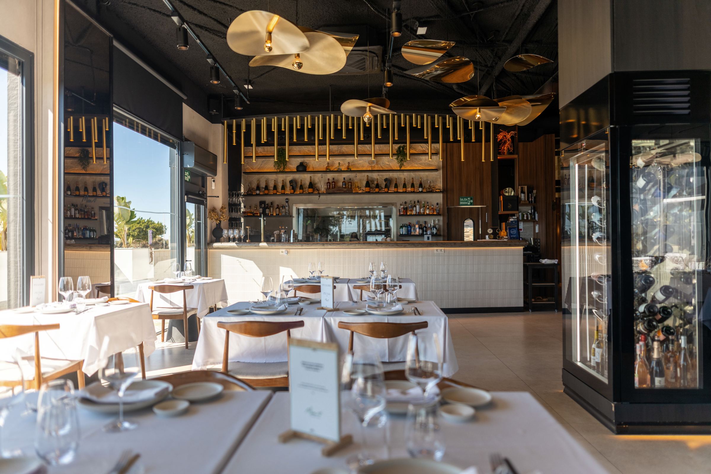 Comedor de Mimo con lámparas doradas en forma de hoja, barra al fondo y vinoteca acristalada