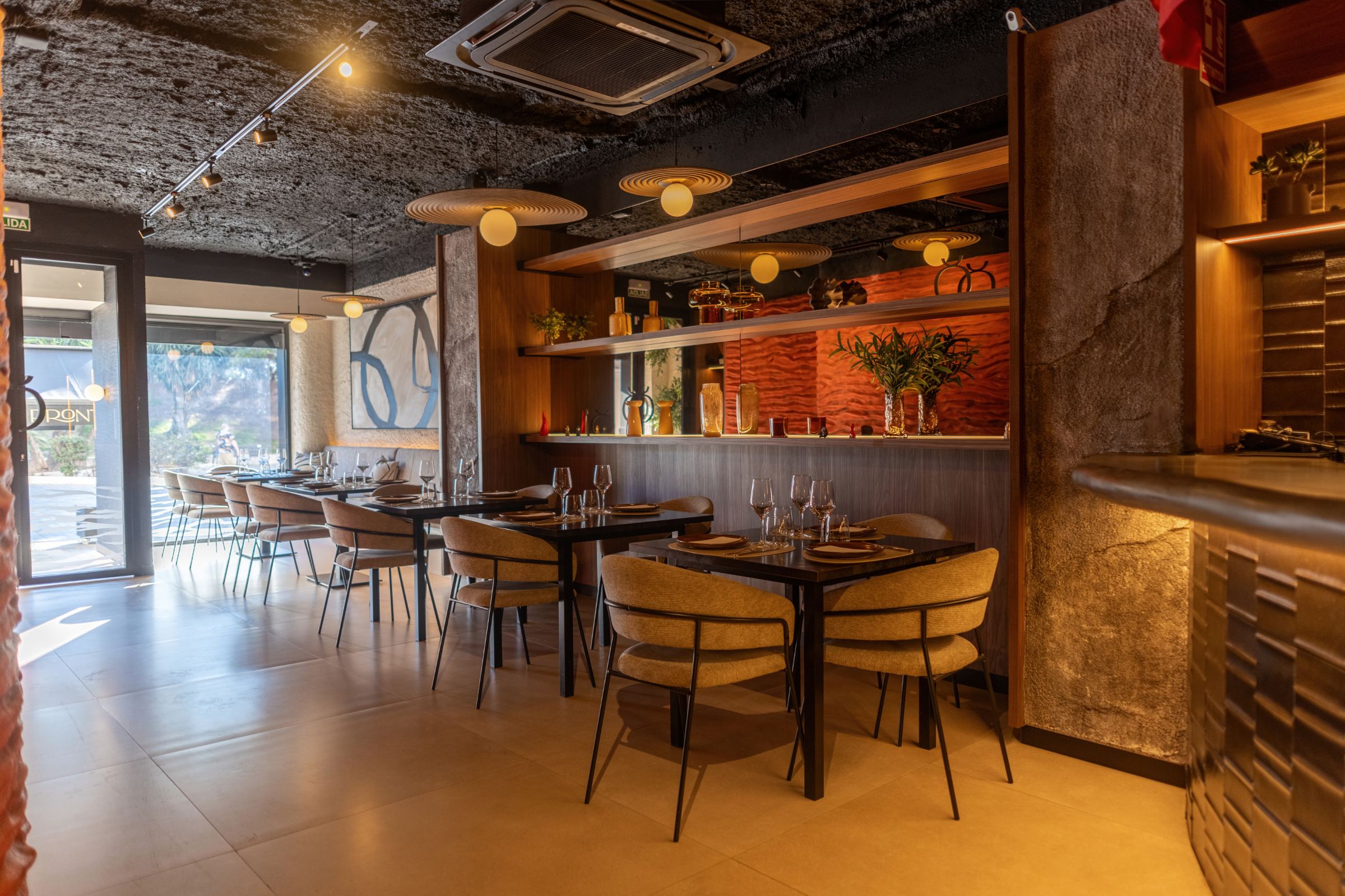 Comedor con mesas oscuras, sillas tapizadas, pilar de piedra y techo oscuro