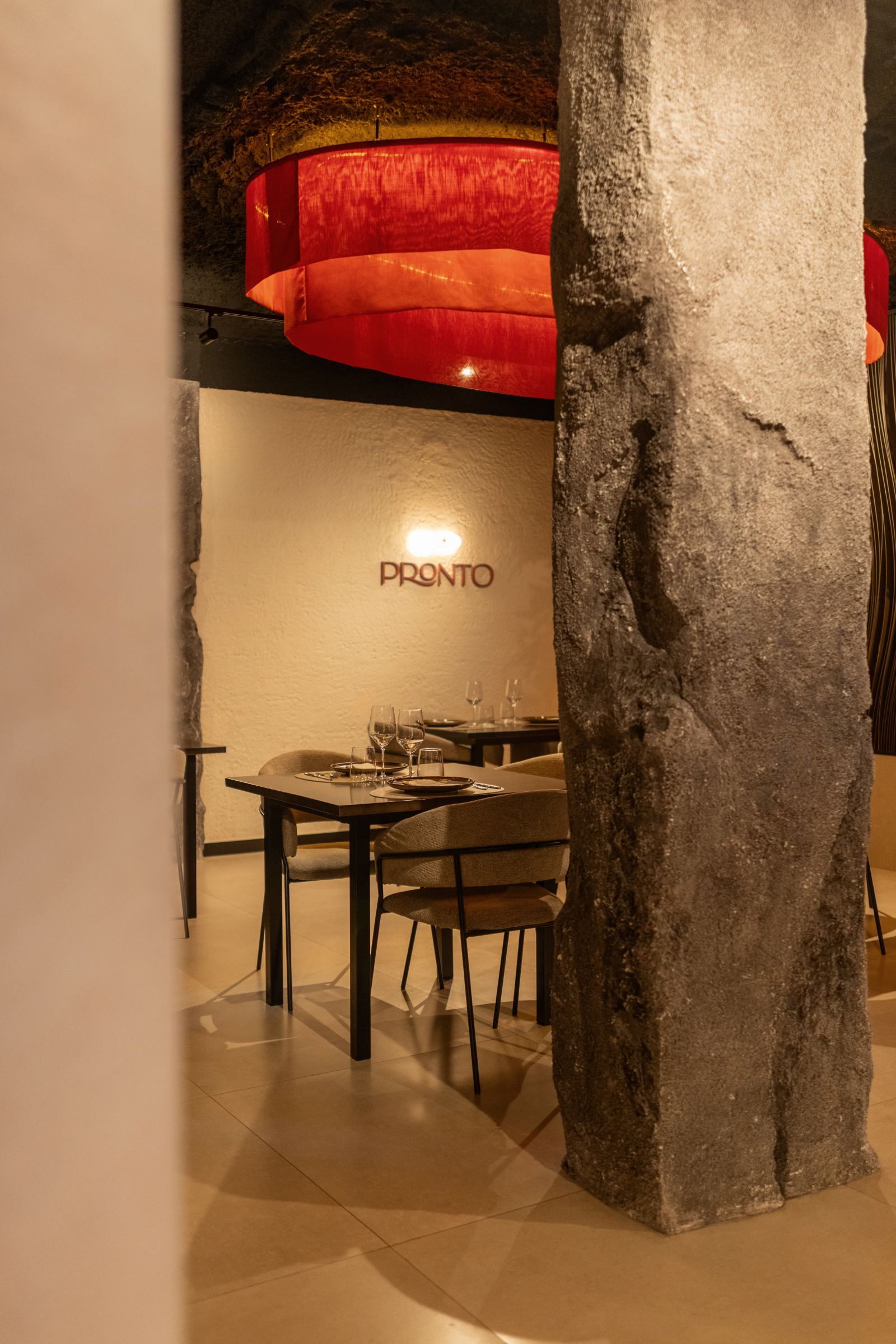 Pilar de piedra natural y lámpara roja suspendida sobre el comedor, con el logotipo de Pronto al fondo