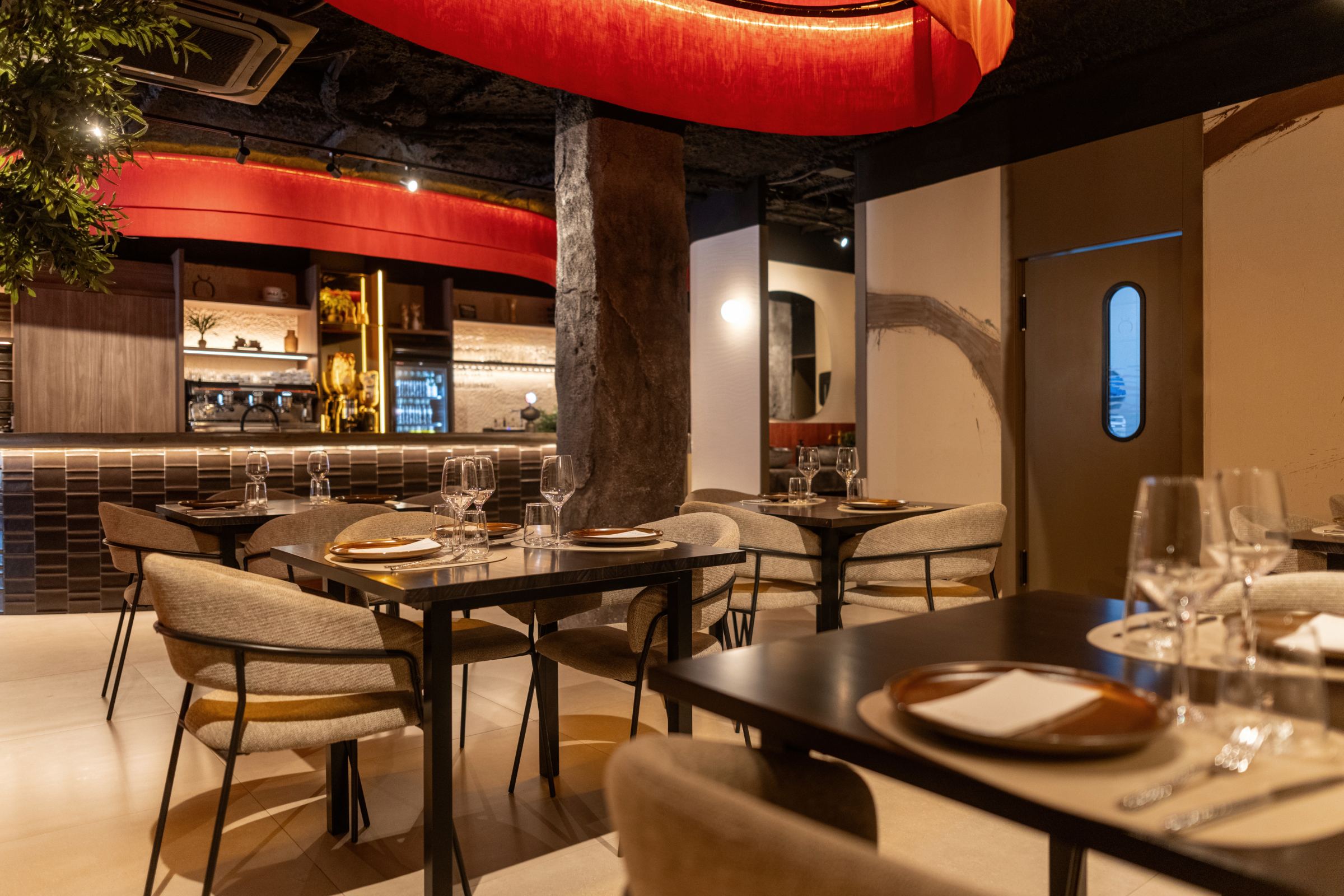 Vista del comedor hacia la barra, con lámparas rojas y pilar de piedra