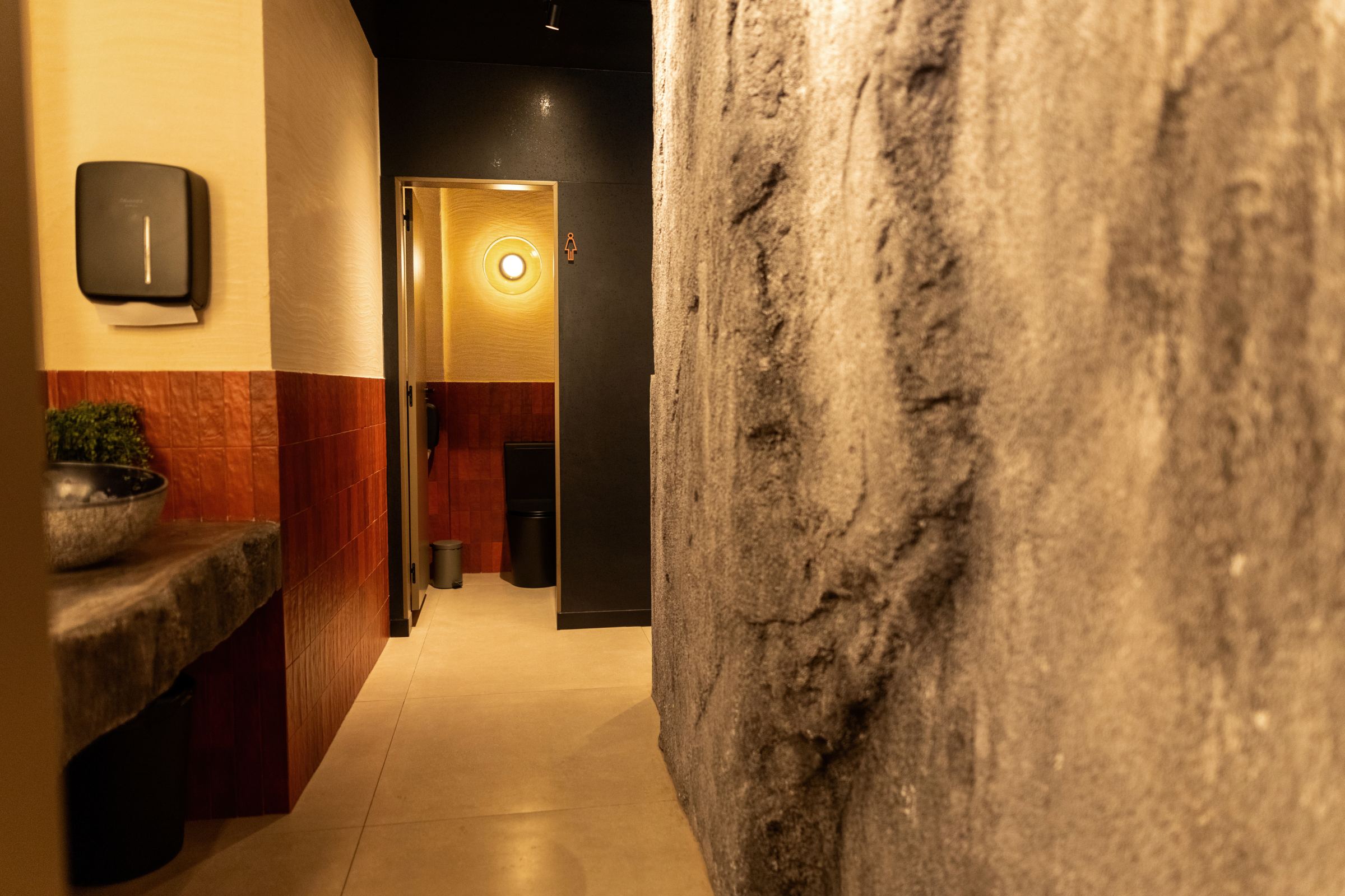 Acceso a los aseos entre una pared de piedra y un zócalo rojo